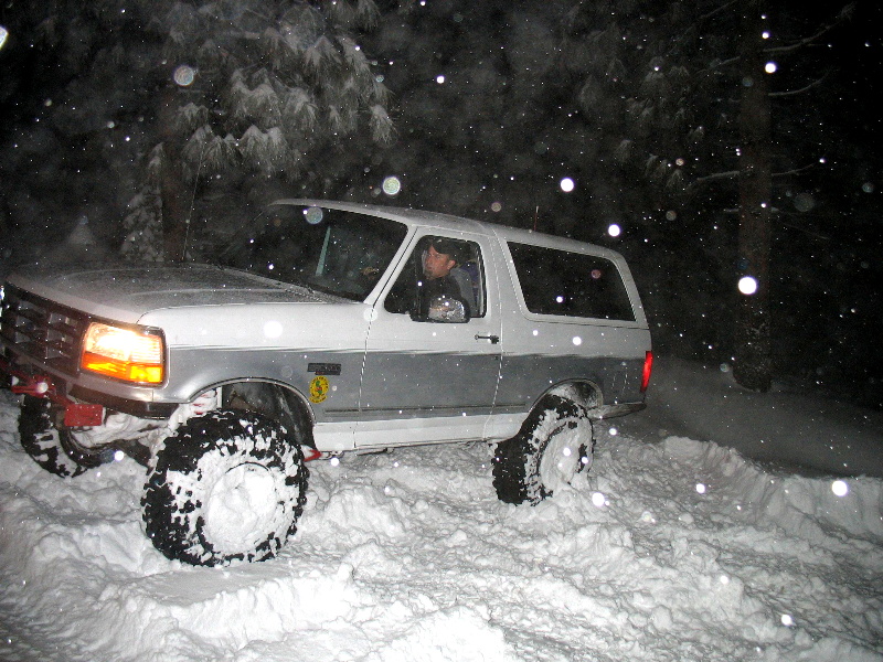 White and grey 1996 Ford Bronco driving through deep snow at night