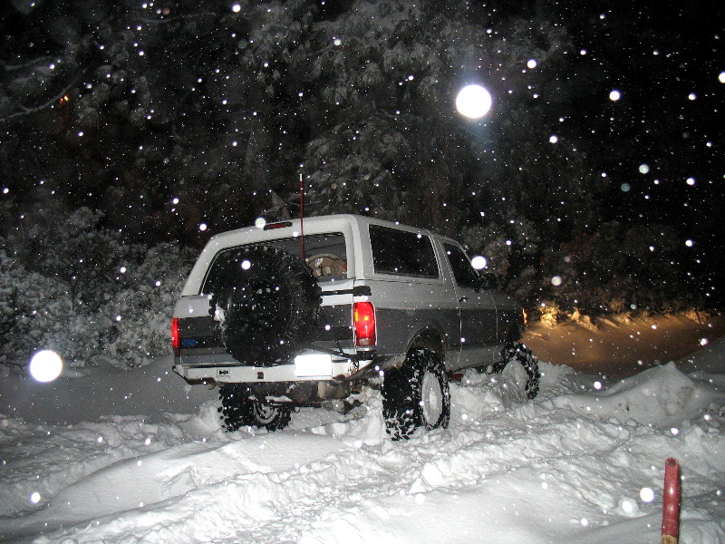 1996 Ford Bronco driving on a snowy road at night, rear view