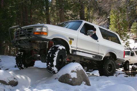 1996 Ford Bronco - A white 1996 Ford Bronco navigates a snowy trail, its large tires gripping rocks.