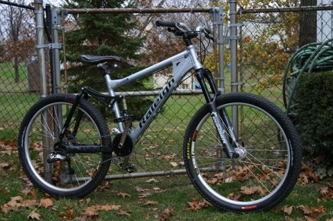1997 Ford Probe - A silver Raleigh bicycle with full suspension is shown parked outdoors next to a fence.