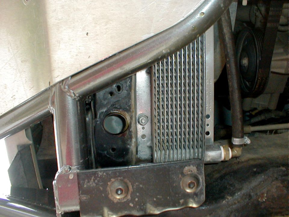 Close-up of a vehicle's engine bay showing a radiator, metal tubing, and a black drive belt