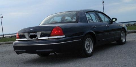 2000 Ford Crown Victoria - A black 2000 Ford Crown Victoria is parked outdoors with a body of water in the background.
