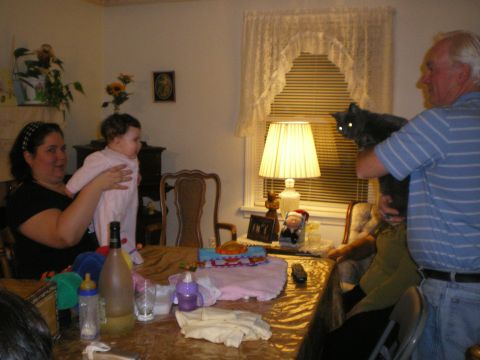 2000 Ford Crown Victoria - A family is gathered around a table, with a woman holding a baby and a man holding a cat.