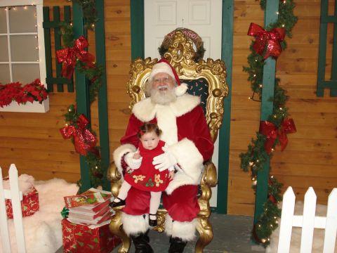 2000 Ford Crown Victoria - Santa Claus holds a baby on his lap while seated on a throne, surrounded by Christmas decorations.