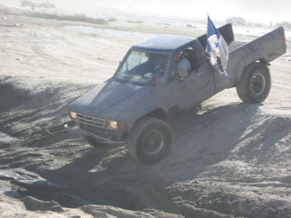 Toyota pickup truck with a flag in the bed driving on a dirt hill