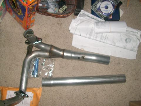 1989 Ford Bronco - An exhaust Y-pipe and straight pipe are laid out on the floor with various documents and a basket in the background.