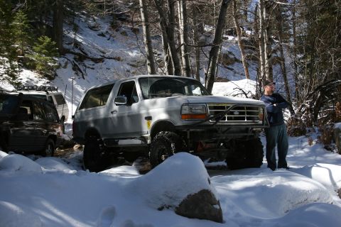 1996 Ford Bronco - A modified Ford Bronco sits in the snow with a man standing next to it in a wooded area.