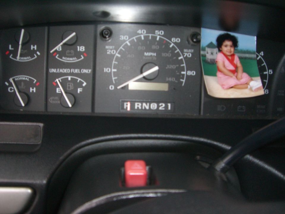 1994 Ford Bronco interior dashboard with fuel and temperature gauges, speedometer, and a photo of a child