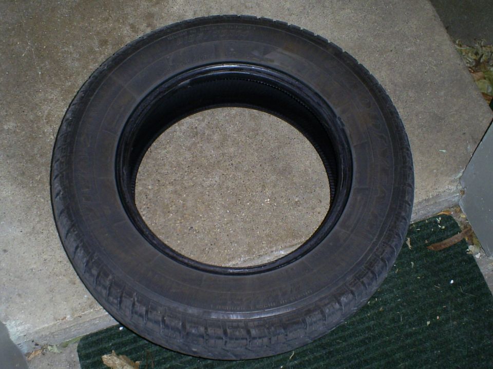 single tire is shown on a concrete surface with a green mat. Text on the tire is not legible