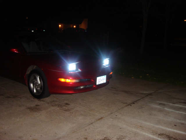 Red 1995 Ford Probe with pop-up headlights on at night