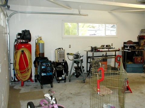 1996 Ford Bronco - A cluttered garage workshop contains various tools and equipment, including welding machines and an air compressor.