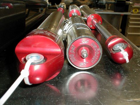 1996 Ford Bronco - Three red and chrome nitrogen shock absorbers are displayed, one with a visible 200 psi marking.