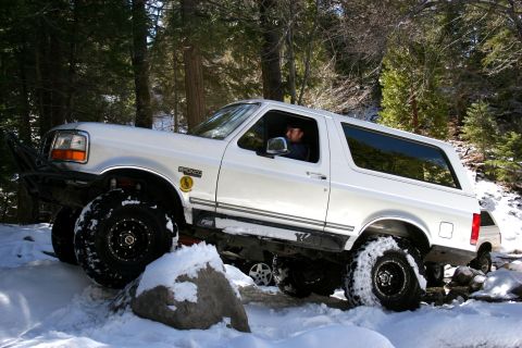 1996 Ford Bronco - A white 1996 Ford Bronco navigates a snowy trail with large off-road tires.