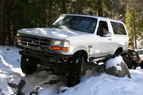1996 Ford Bronco - A white 1996 Ford Bronco tackles a snowy, rocky trail, demonstrating its off-road capabilities.