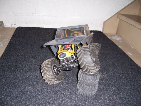 1996 Ford Bronco - A remote control monster truck sits on a dark carpeted surface with a concrete wall and stairs in the background.
