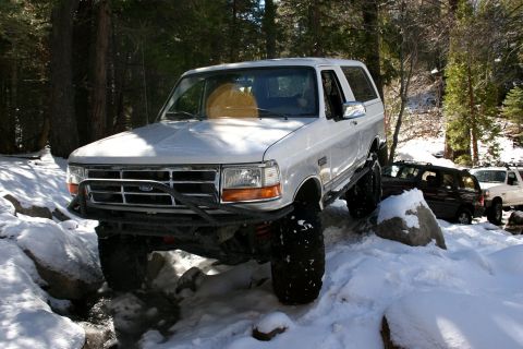 1996 Ford Bronco - A lifted 1996 Ford Bronco tackles a snowy, rocky trail, with two other vehicles visible in the background.
