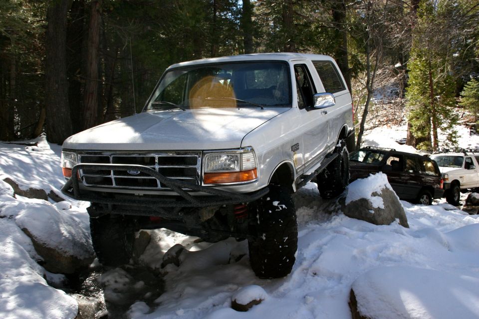 White 1996 Ford Bronco navigating snowy terrain with other vehicles behind