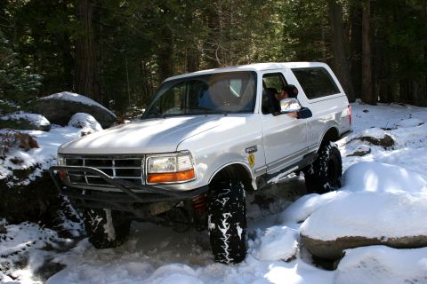 1996 Ford Bronco - White 1996 Ford Bronco navigates a snowy trail with large rocks.