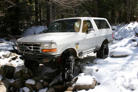 1996 Ford Bronco - This 1996 Ford Bronco is shown off-roading on a snowy path with rocks and trees.