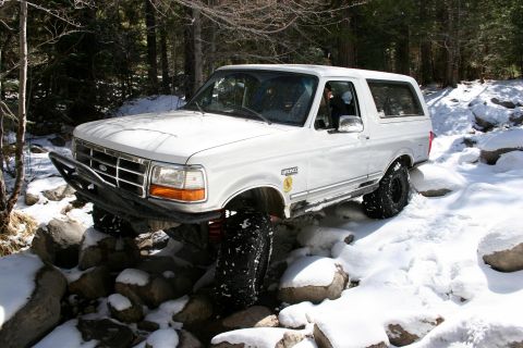 1996 Ford Bronco - A white 1996 Ford Bronco is shown off-roading through a snowy, rocky terrain.