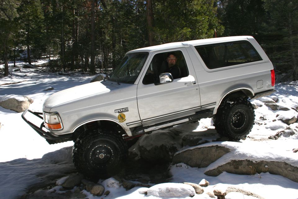 White Ford Bronco with off-road tires navigating rocks and snow