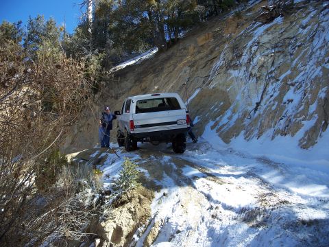 1996 Ford Bronco - A white 1996 Ford Bronco navigates a challenging snowy and rocky path, with two people assisting.