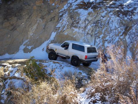1996 Ford Bronco - White 1996 Ford Bronco navigates a snowy, off-road trail next to a rock face.
