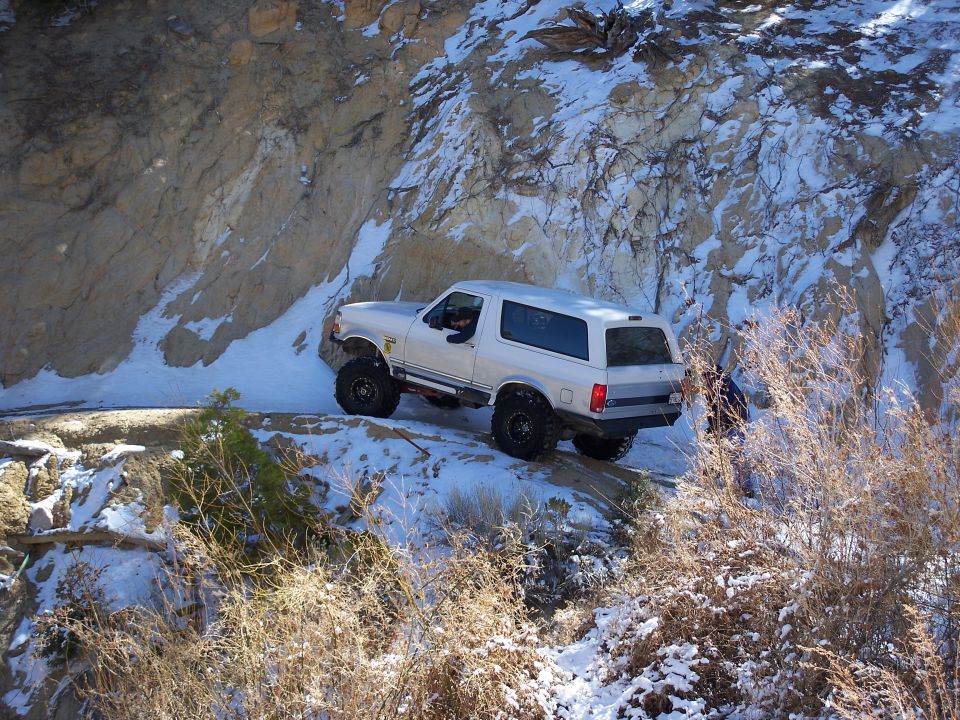 1996 Ford Bronco driving on a snowy mountain road with rocky cliffs