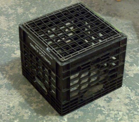 1994 Ford Bronco - A black plastic milk crate with a metal grate on top sits on a concrete floor.