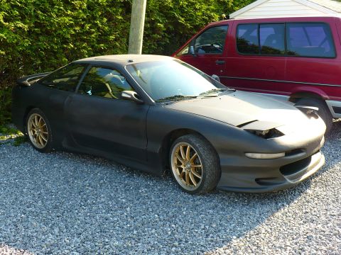 1993 Ford Probe - This 1993 Ford Probe is seen in a three-quarter front view, parked on a gravel surface next to a red van.