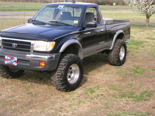 Black Toyota single-cab pickup, lifted on large tires, parked on grass