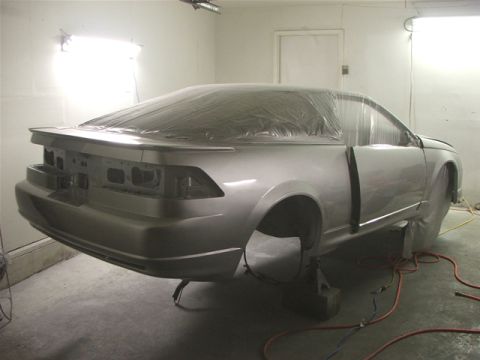 1991 Ford Probe - A car is being prepped for painting, with plastic sheeting covering most of its body and no wheels attached.
