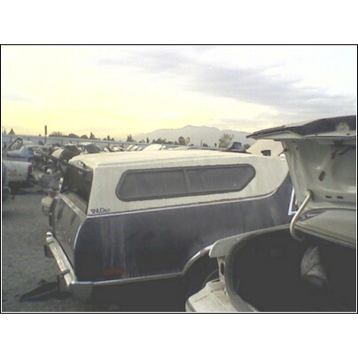 1973 Ford Ranchero - A junkyard scene with multiple vehicles, including a pickup truck fitted with a camper shell.