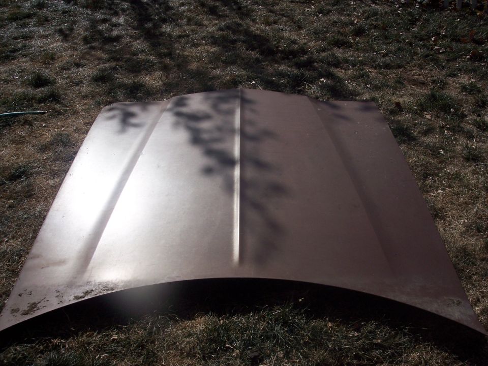 Brown car hood with a central crease, lying on grass