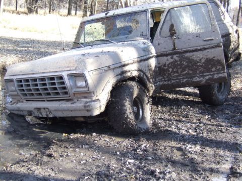1989 Ford Bronco - A heavily muddied 1978 Ford Bronco is stuck in a muddy, watery area with its driver's door ajar.