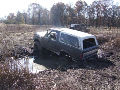 1989 Ford Bronco - A Ford Bronco is stuck in a muddy field, with a second off-road vehicle visible behind it.