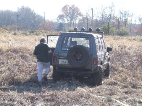 1989 Ford Bronco - A man approaches a mud-covered SUV with its rear door open, stuck in a field of dry grass.