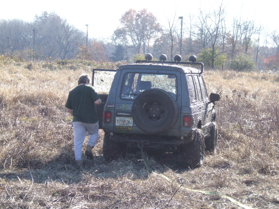 Guy getting into a muddy SUV with a spare tire on the back, stuck in a field