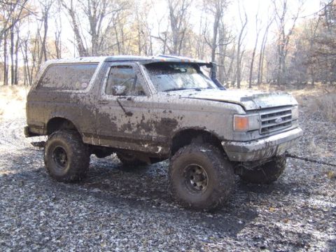 1989 Ford Bronco - This heavily mud-splattered 1987 Ford Bronco is shown from a 3/4 front angle in a wooded area.