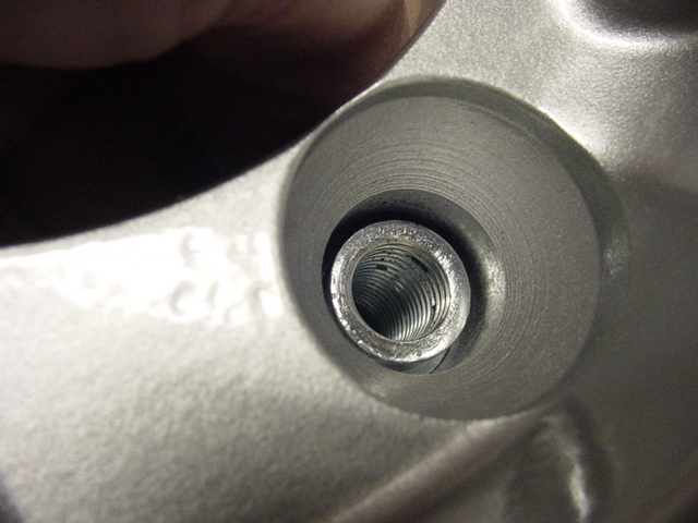 Close-up of a lug hole and threaded sleeve on a silver alloy wheel