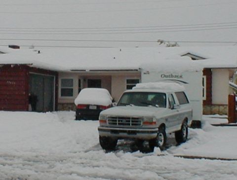 1996 Ford Bronco - A silver Ford Bronco is parked in a snowy driveway next to a house and another car.