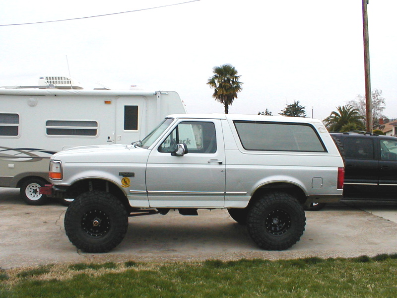 Lifted silver Ford Bronco parked next to a trailer and a black SUV
