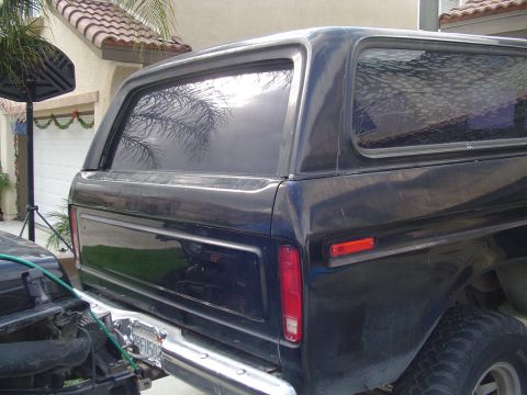 1978 Ford Bronco - Rear view of a dark blue 1978 Ford Bronco, showing its quarter panel and tailgate. Another vehicle is partially visible to the left.