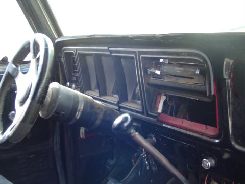 1978 Ford Bronco - The dashboard of an older vehicle shows a steering wheel, air vents, and an open radio slot.