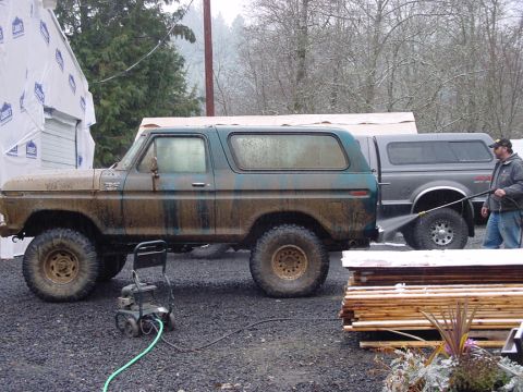 1979 Ford Bronco - A man pressure washes a muddy 1978 Ford Bronco next to a pickup truck on a cloudy day.