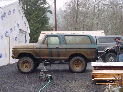 1979 Ford Bronco - A muddy teal Ford Bronco is parked next to a pickup truck while a man washes it.