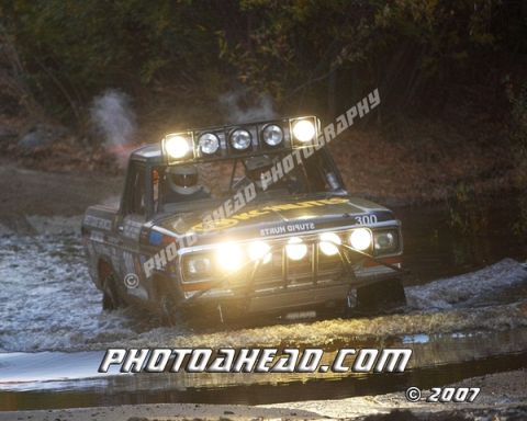 1996 Ford Bronco - This off-road truck navigates a water obstacle, its powerful lights cutting through the dim surroundings.