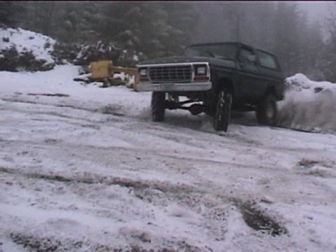 1979 Ford Bronco - A 1979 Ford Bronco navigates a snowy terrain, kicking up snow as it drives.