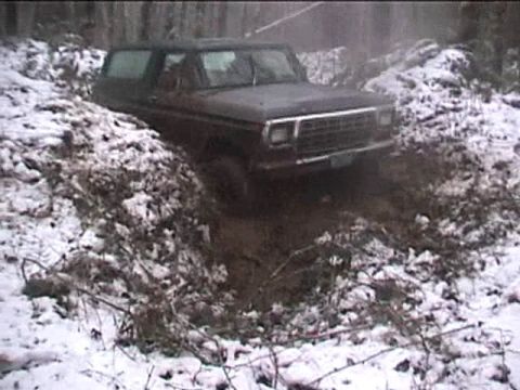 1979 Ford Bronco - A Ford Bronco is stuck in a muddy ditch with snow on the ground and trees in the background.