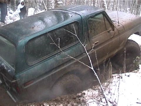 1979 Ford Bronco - A muddy green Ford Bronco is stuck in a snowy, wooded area.